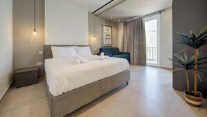 A modern hotel room with a large bed, a small seating area, and a balcony with a view. - Seafront Seafront 3BR home in Qawra w/WIFI & AC (San Pawl il-Baħar)