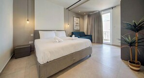 A modern hotel room with a large bed, a small seating area, and a balcony with a view. - Seafront Seafront 3BR home in Qawra w/WIFI & AC (San Pawl il-Baħar)