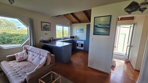 A modern kitchen with a central island, a dining area with a sofa, and a view through a window.
