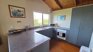 A kitchen with a granite countertop, a sink, a microwave, and a stove. There is a window with blinds, a painting on the wall, and a ceiling with wooden beams.