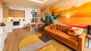 Eine moderne Küche mit Holzausstattung, ein Essbereich mit bunten Stühlen, ein braunes Ledersofa und ein leuchtendes Sonnenuntergangsmotiv an der Wand.