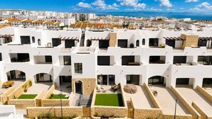 Ein moderner Wohnkomplex mit mehreren weißen Gebäuden, Außenveranden und Blick aufs Meer.