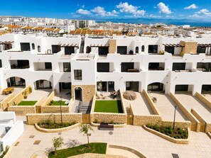 Ein moderner Wohnkomplex mit mehreren weißen Gebäuden, Außenveranden und Blick aufs Meer.