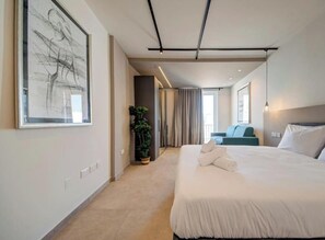 A modern hotel room with a large bed, a potted plant, a view of the city, and a large abstract painting on the wall. - Exceptional 2BR seafront home in Qawra w/WIFI & AC (San Pawl il-Baħar)