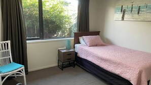 A bedroom with a bed, a chair, a nightstand, a window with curtains, and a painting on the wall.