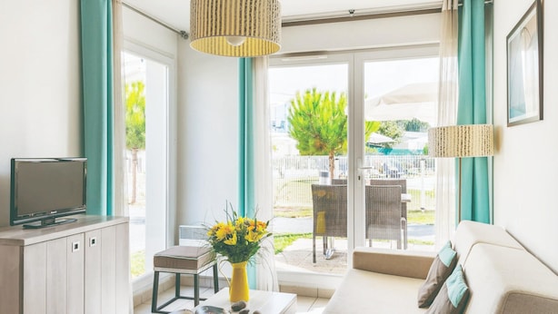 Ein modernes Wohnzimmer mit einer Couch, einem Fernseher, einem Couchtisch mit Büchern und einer Blumenvase sowie einem Balkon mit Gartenmöbeln.