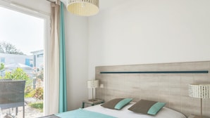 Ein Hotelzimmer mit einem Bett, zwei Nachttischen, einem Sessel und Blick nach draußen.