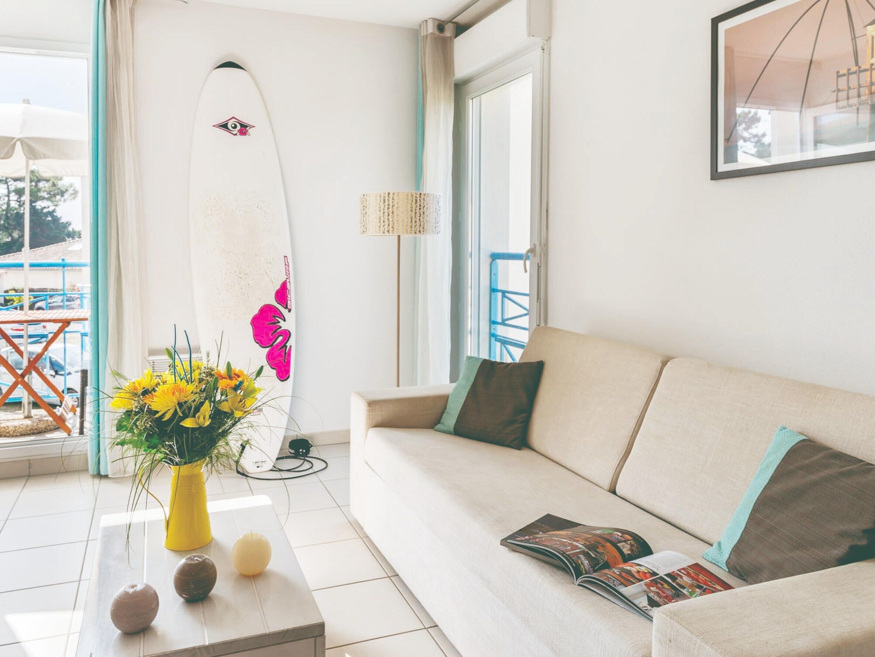 A living room with a sofa, a coffee table with decorative items, a surfboard, and a window with a view.