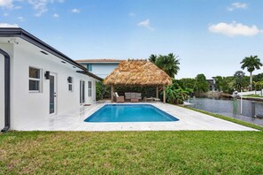 Ein Pool mit einer strohgedeckten Konstruktion, ein weißes Gebäude und eine Wasserspielelement.