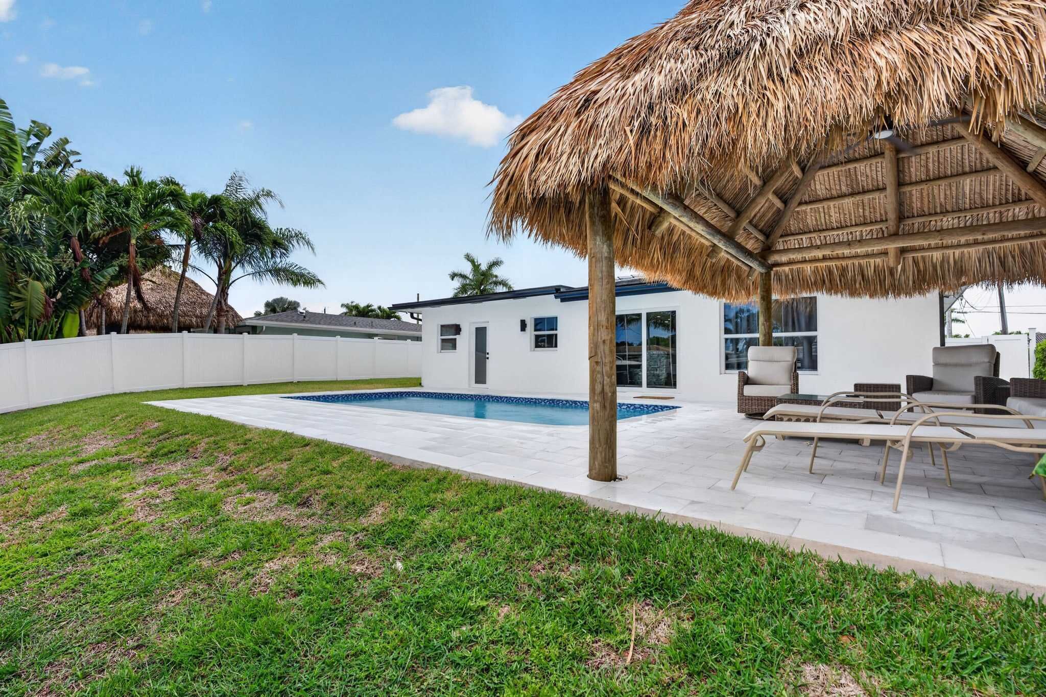 A modern house with a pool, outdoor furniture, and a thatched roof structure.