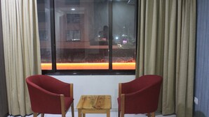 Quarto com duas cadeiras vermelhas, uma mesa de madeira pequena e uma janela com cortinas.