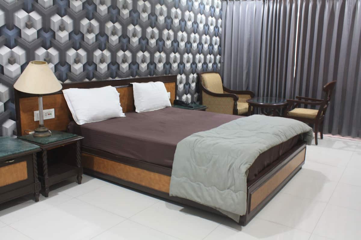 Habitación de hotel ordenada con cama, una silla, una mesita y una lámpara.