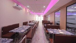Restaurante com várias mesas e cabines, teto com iluminação rosa e uma janela grande à direita.