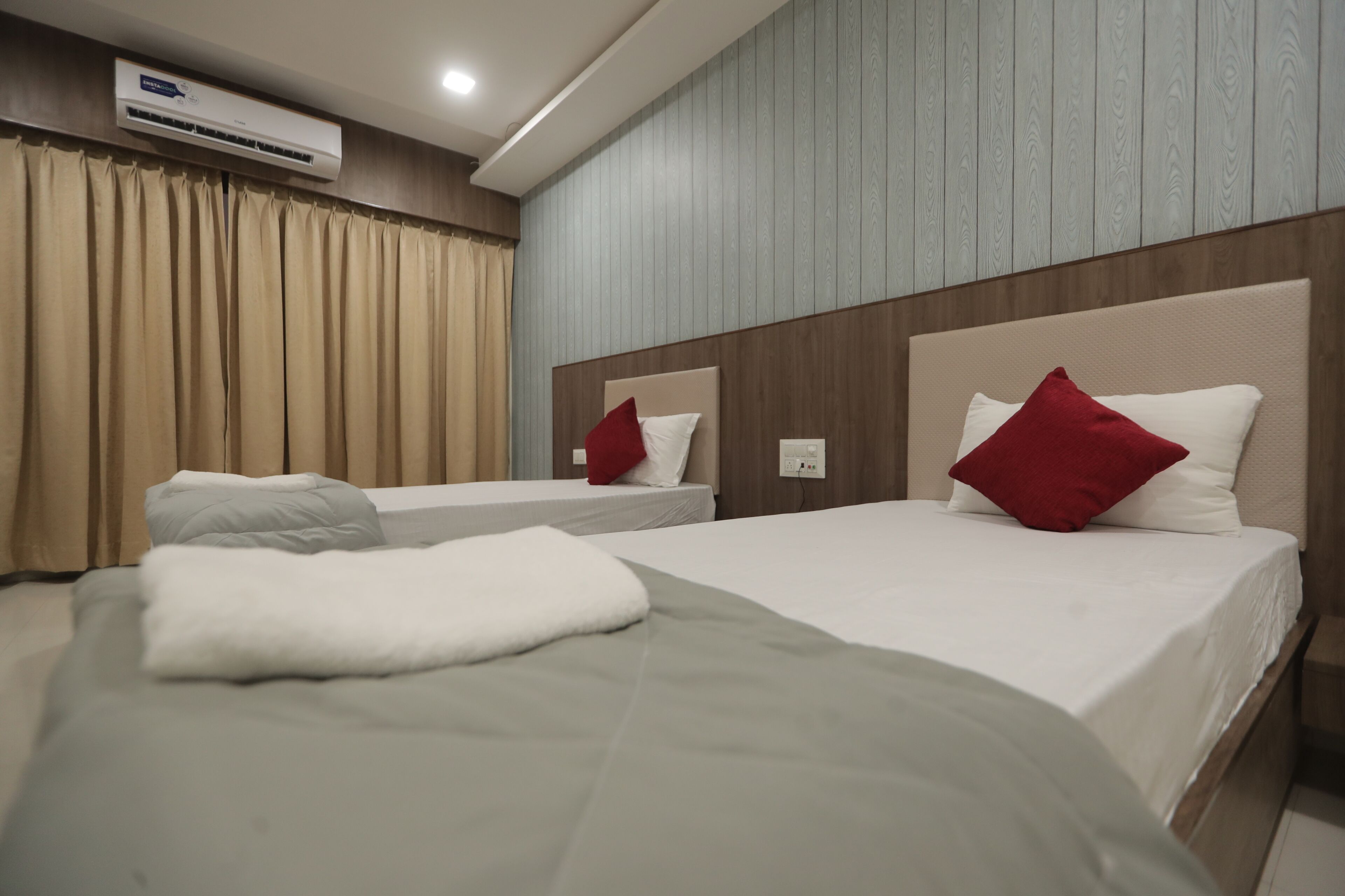 Een hotelkamer met twee bedden, beige gordijnen, een houten hoofdbord en een airconditioning.