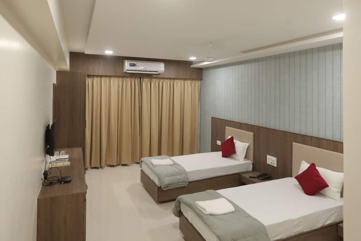 Habitación de hotel con dos camas, un televisor de pantalla plana, una mesita de noche de madera y un equipo de aire acondicionado.