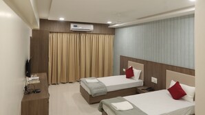 Quarto de hotel com duas camas, uma televisão de tela plana, uma mesa de cabeceira de madeira e um aparelho de ar condicionado.