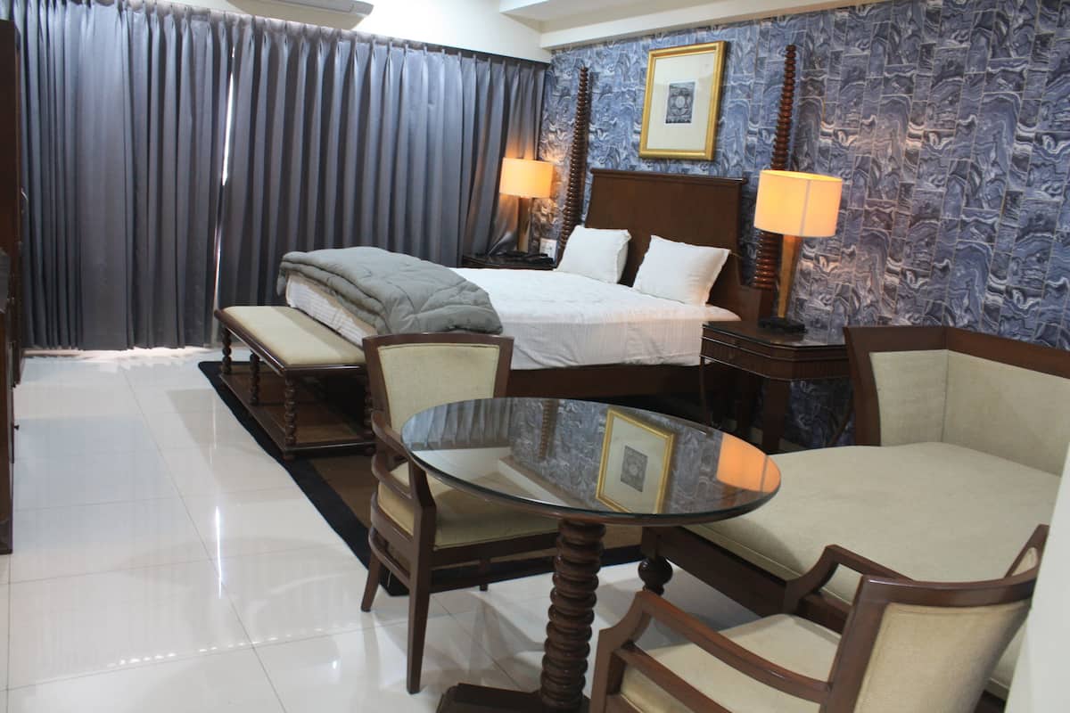Habitación de hotel con una cama, dos mesitas de noche con lámparas, una mesa redonda de cristal y dos sillones.
