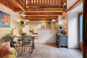 A rustic kitchen with wooden beams, a dining table with chairs, a radiator, and a window.