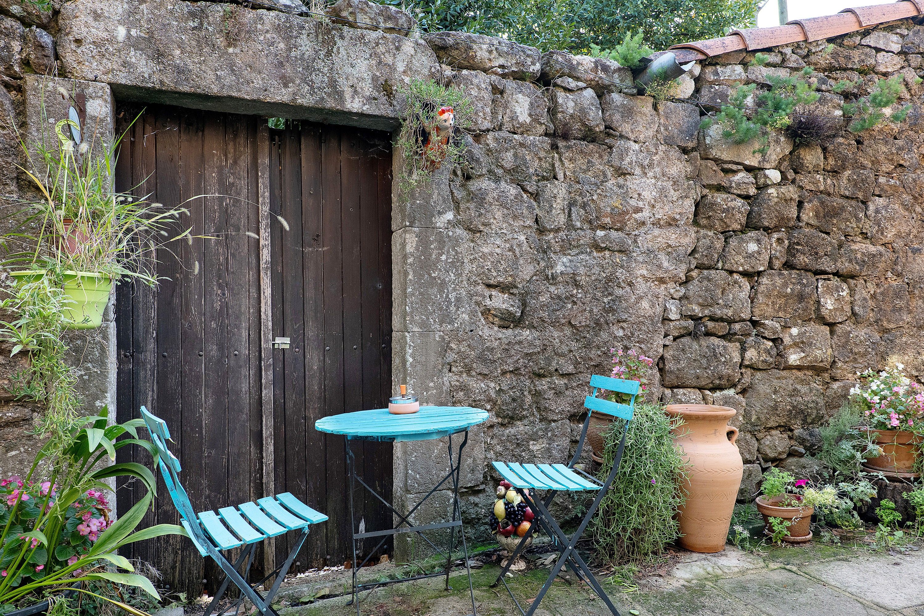 Un espacio de estar al aire libre rústico con puerta de madera, pared de piedra y plantas en macetas.
