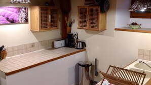 A kitchen with wooden cabinets, a toaster, a coffee maker, and a hanging pot rack. - Holiday Home 'La Fée Du Val - Cottage in Ardèche' with Private Pool, Wi-Fi and Air Conditioning (Rosières)