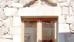 A stone building with a wooden door, potted plants, and a window with a reflection. - Holiday Home 'La Fée Du Val - Cottage in Ardèche' with Private Pool, Wi-Fi and Air Conditioning (Rosières)