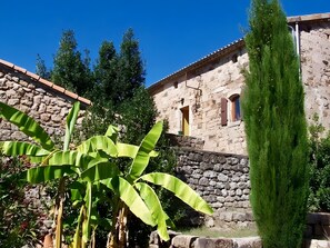 A stone building with a tiled roof, a stone wall, and a tall green plant in the foreground. - Holiday Home 'La Fée Du Val - Cottage in Ardèche' with Private Pool, Wi-Fi and Air Conditioning (Rosières)
