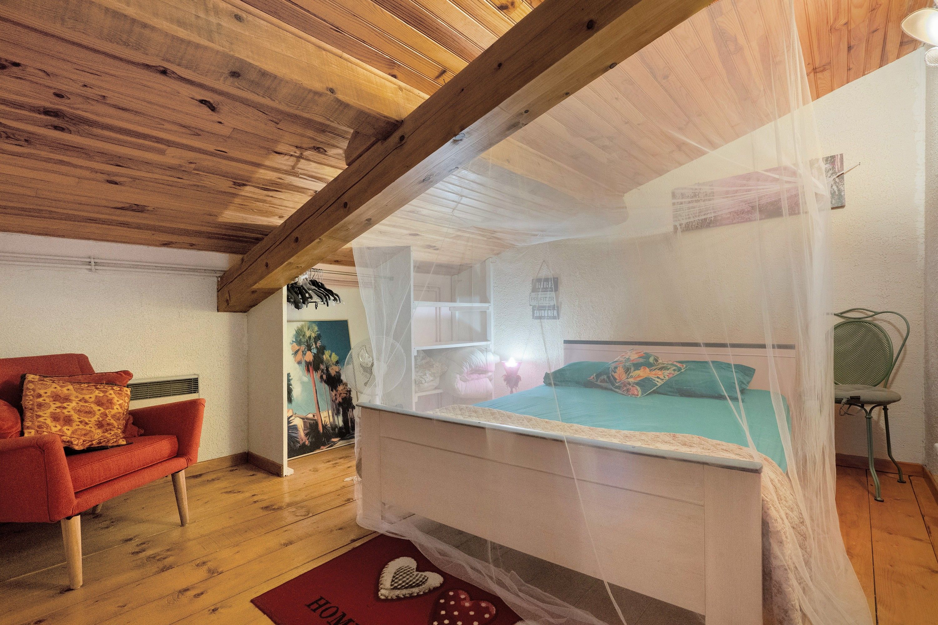 Un dormitorio con techo de madera, una cama con mosquitero, una silla roja y una silla verde.