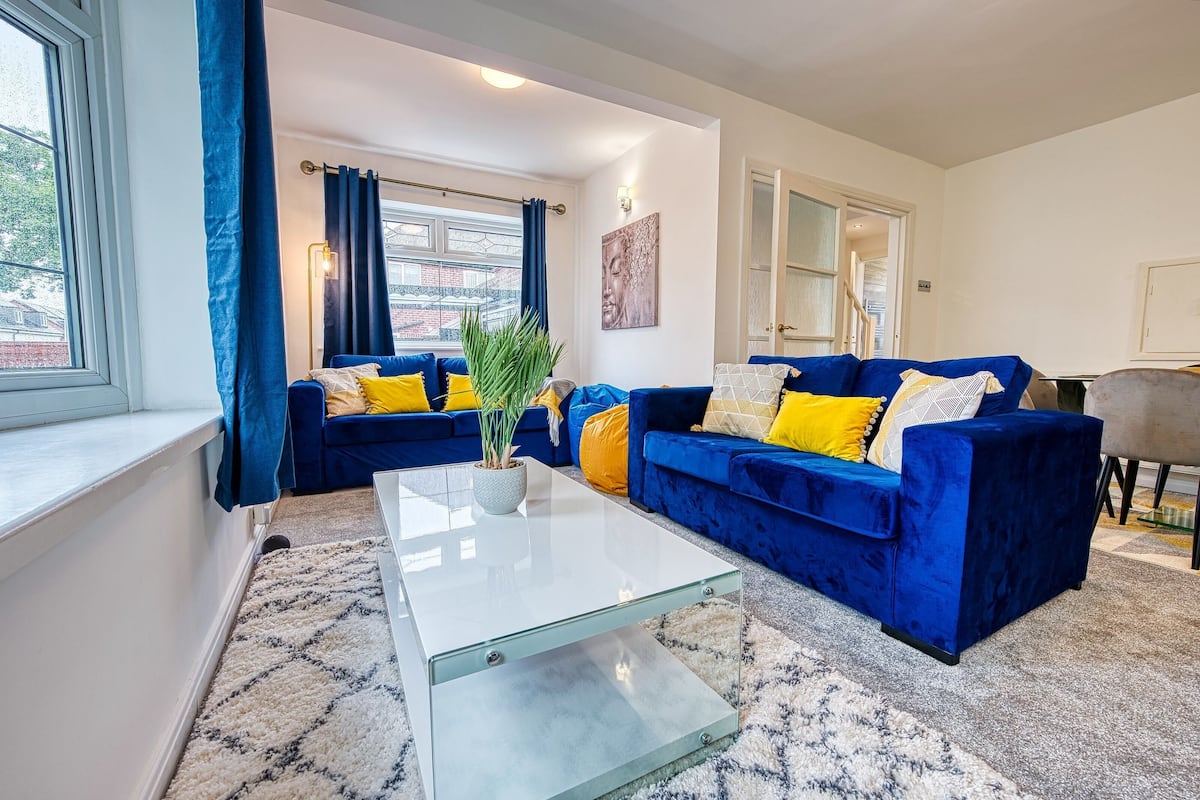 A living room with a blue sofa set, a white coffee table, and a potted plant.