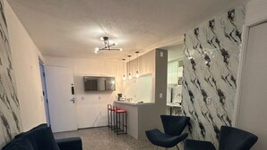 A modern living room with a dark-colored sofa, two armchairs, a kitchen area with a bar counter, and a dining table. - Atlantico 204 apartment, 50m2, 1 bedroom, sleeps up to 4 people. (Fortaleza)