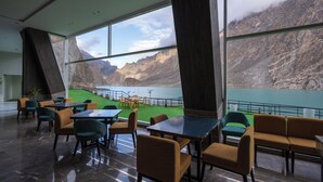 A modern interior with large windows offering a view of a mountainous landscape and a lake. - Pearl Continental Attabad Lake (Aina Abad)