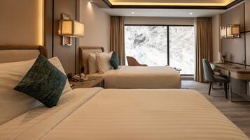 A hotel room with two beds, a desk, a chair, and a large window with curtains.