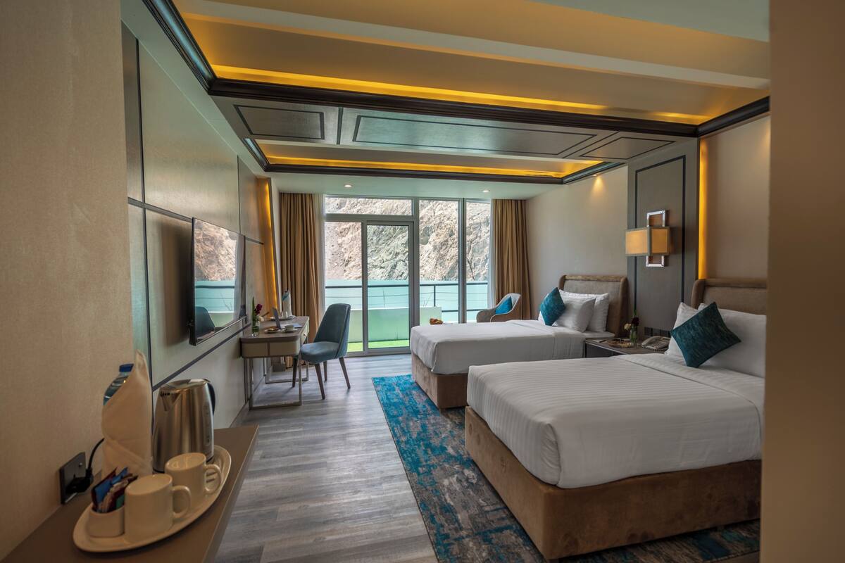 Habitación de hotel con dos camas, un escritorio, una silla, un televisor y vistas al exterior.