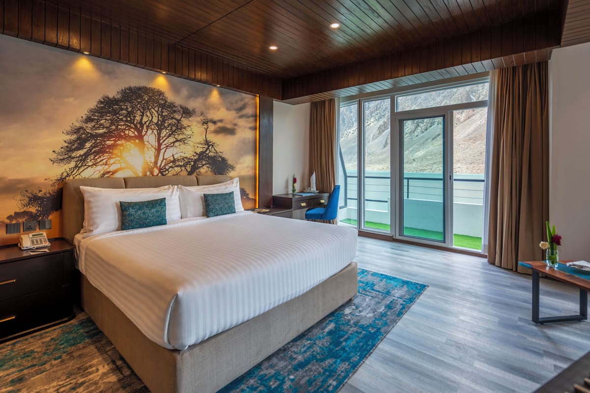 Una cama grande con vistas al exterior, un escritorio y una silla en una habitación con paneles de madera y un ventanal amplio.