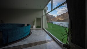 A modern interior with a large window, a blue sofa, and a potted plant. - Pearl Continental Attabad Lake (Aina Abad)