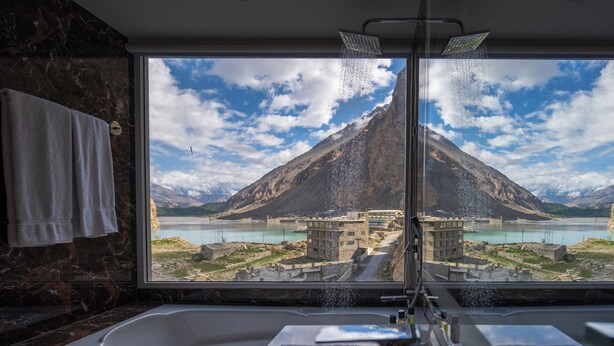 A bathroom with a large window, a bathtub, and a showerhead. - Pearl Continental Attabad Lake (Aina Abad)