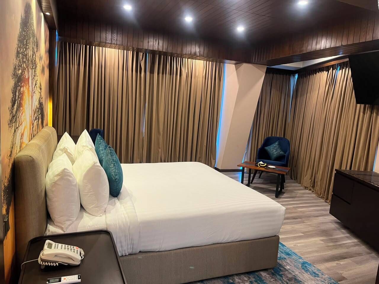 A hotel room with a large bed, a desk with a telephone, a chair, and a TV mounted on the wall.