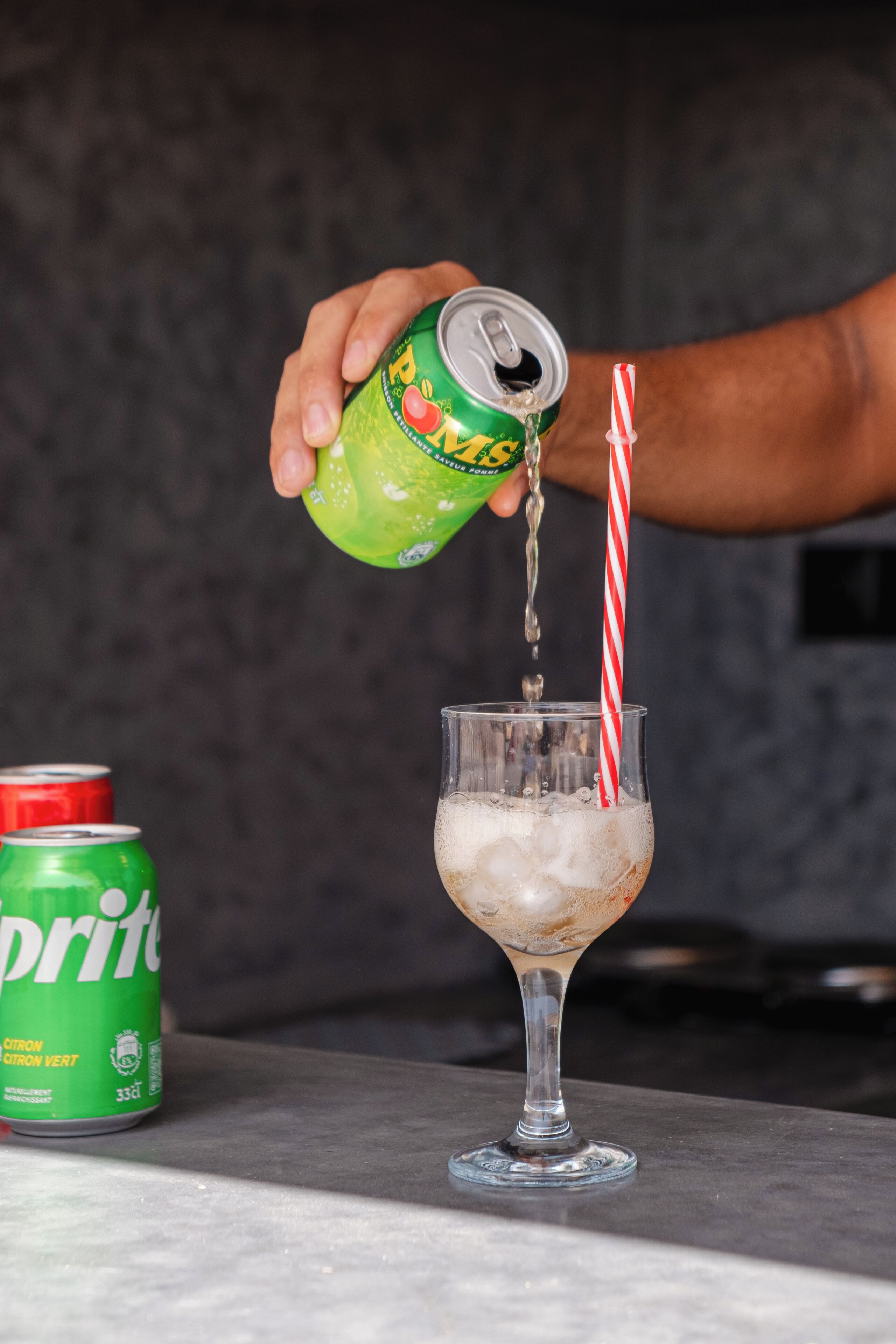 A hand pouring a beverage from a can into a glass with a straw.