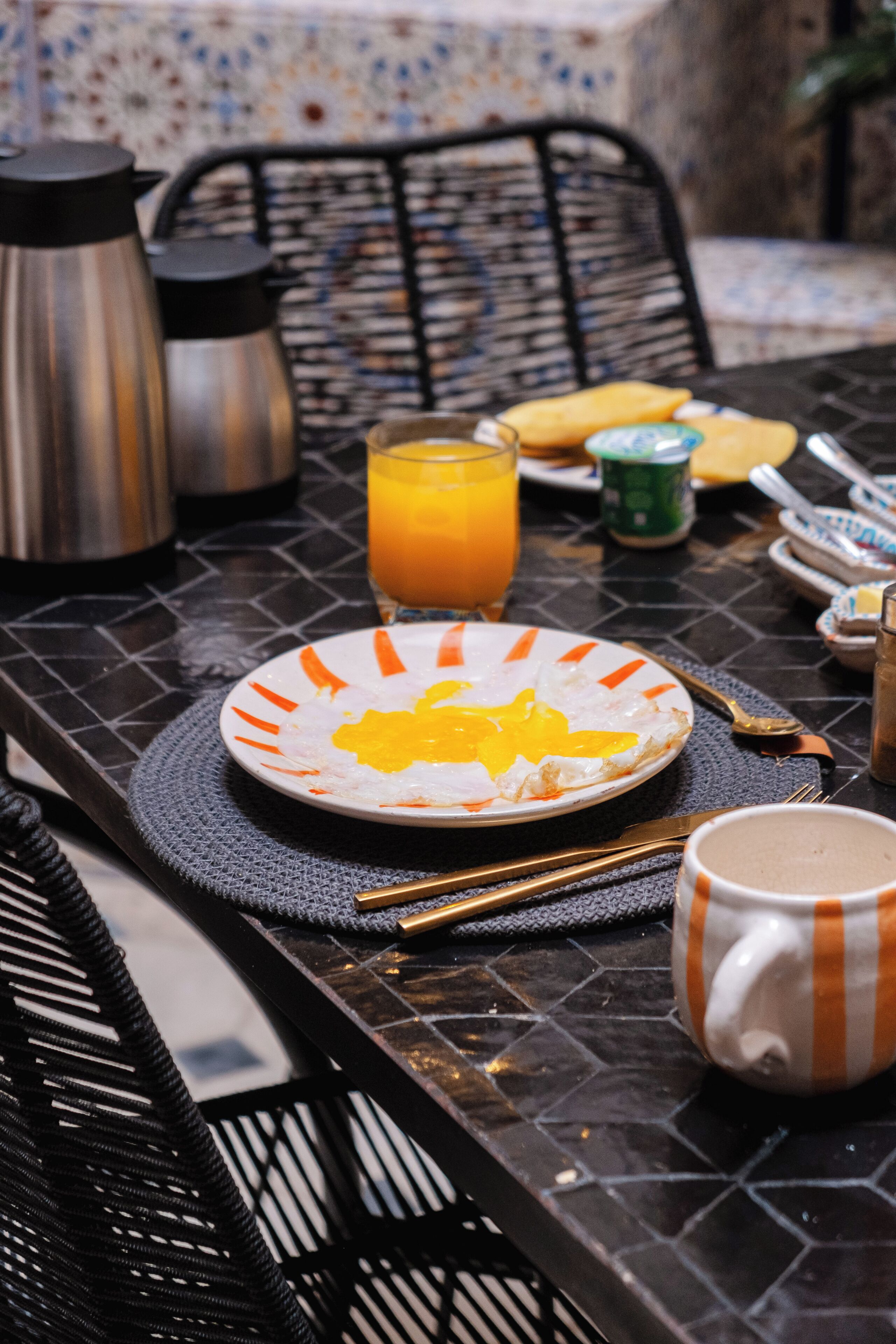 Een ontbijttafel met eten op een bord, een glas sinaasappelsap, een koffiemok en een thermosfles.