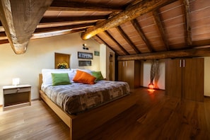 Ein Schlafzimmer mit Holzboden, einem Bett mit gemusterten Betttextilien, einem Nachttisch und einem an der Wand befestigten Regal.