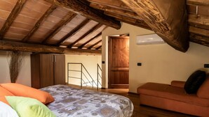 A bedroom with a wooden ceiling, a bed with patterned bedding, a sofa, and a staircase leading to an upper level. - This two-level apartment located in a semi-detached house in the center of Arbia, just a 5-minute drive from Siena, is the ideal starting point for visiting the Crete Senesi, Chianti, and Val d'Orcia. Featuring a parking space, a shared garden with a pat (Arbia)