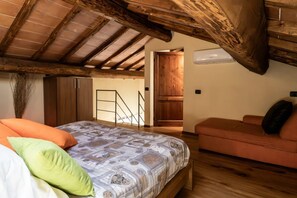 Ein Schlafzimmer mit Holzboden, einem Bett mit gemusterten Betttextilien, einer Couch und einer Treppe, die in ein Obergeschoss führt.