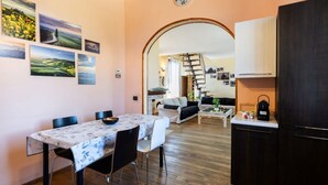 A dining area with a table and chairs, a kitchen with cabinets, and a living area with a sofa and a staircase. - This two-level apartment located in a semi-detached house in the center of Arbia, just a 5-minute drive from Siena, is the ideal starting point for visiting the Crete Senesi, Chianti, and Val d'Orcia. Featuring a parking space, a shared garden with a pat (Arbia)