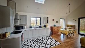 A modern kitchen with white cabinets, a black and white patterned rug, and a dining area with a yellow table and chairs. - Aiteannach (Invergarry)