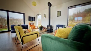 A modern living room with a large window, a fireplace, and a sofa. - Aiteannach (Invergarry)
