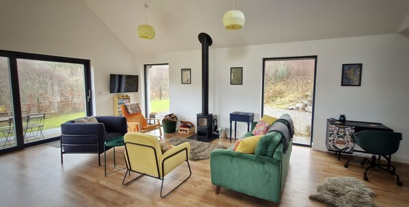 A spacious living room with a large window, a fireplace, and a cozy seating area. - Aiteannach (Invergarry)