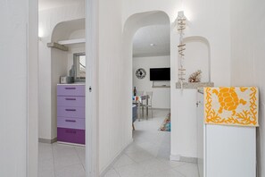 Um corredor com uma cômoda roxa, uma sala de jantar com televisão e um objeto decorativo na parede.