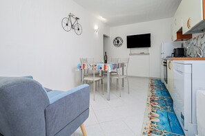 Um espaço compacto para viver com mesa de jantar, cadeiras, sofá, cozinha com fogão e televisão presa na parede.