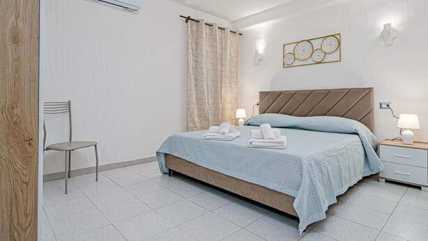Een slaapkamer met een bed, een stoel, een nachtkastje en een wandairconditioner.