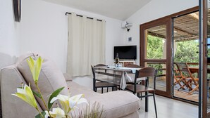 Una sala de estar con sofá, mesa de comedor, sillas, televisor y puerta corrediza de vidrio a una terraza exterior.