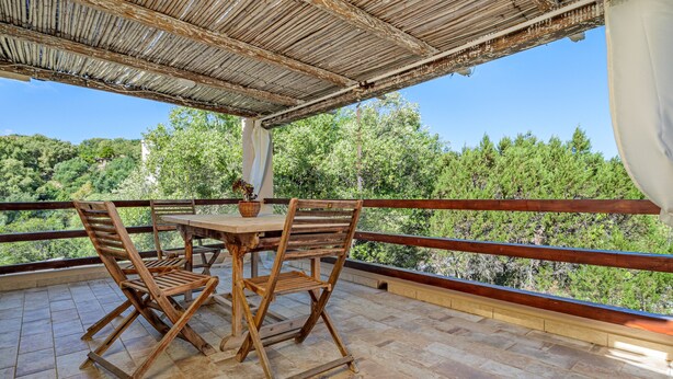 Una mesa y sillas de madera en un balcón con vistas a árboles.